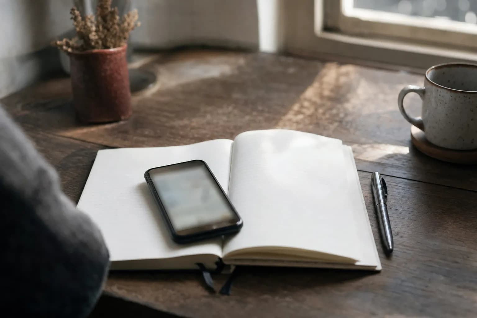 A phone resting on an open notebook on a desk in morning light