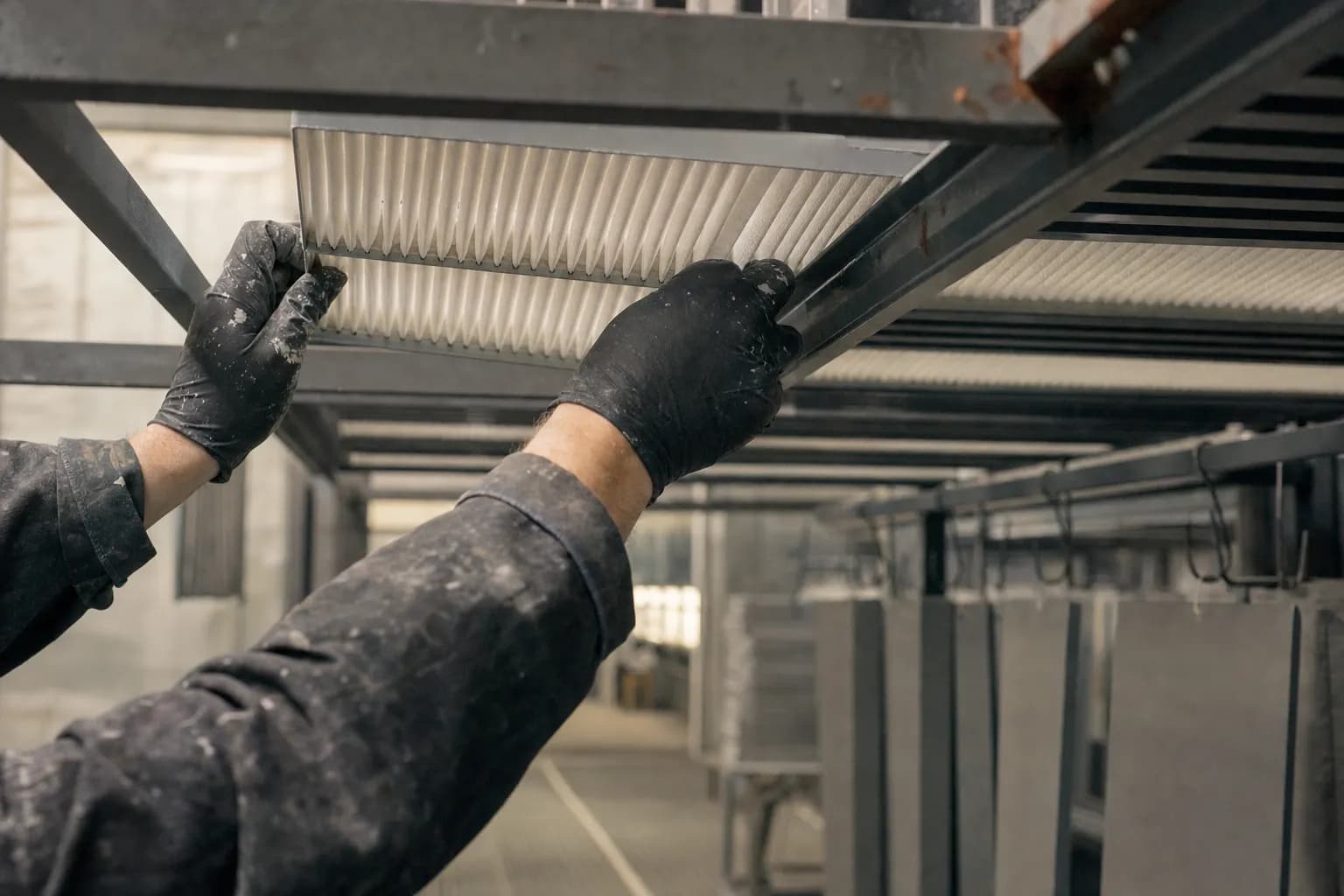 Gloved hands sliding a new intake filter into a paint booth ceiling grid